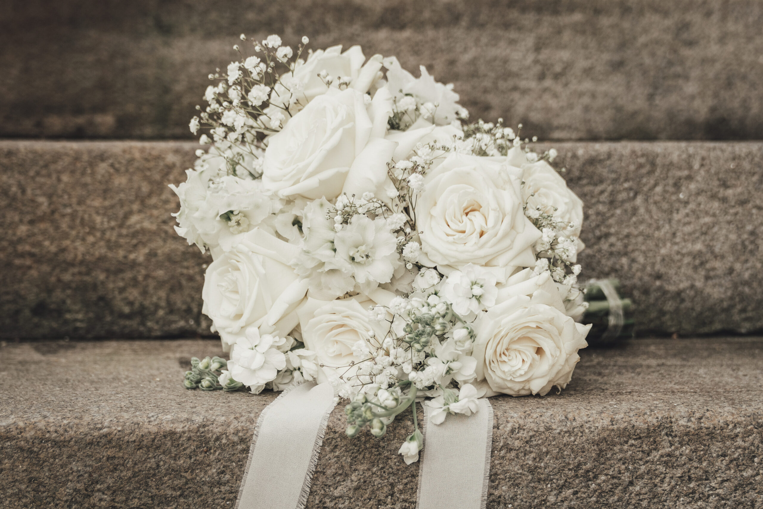 Klassischer weißer Brautstrauß mit Rosen und Schleifenband auf einer Steintreppe