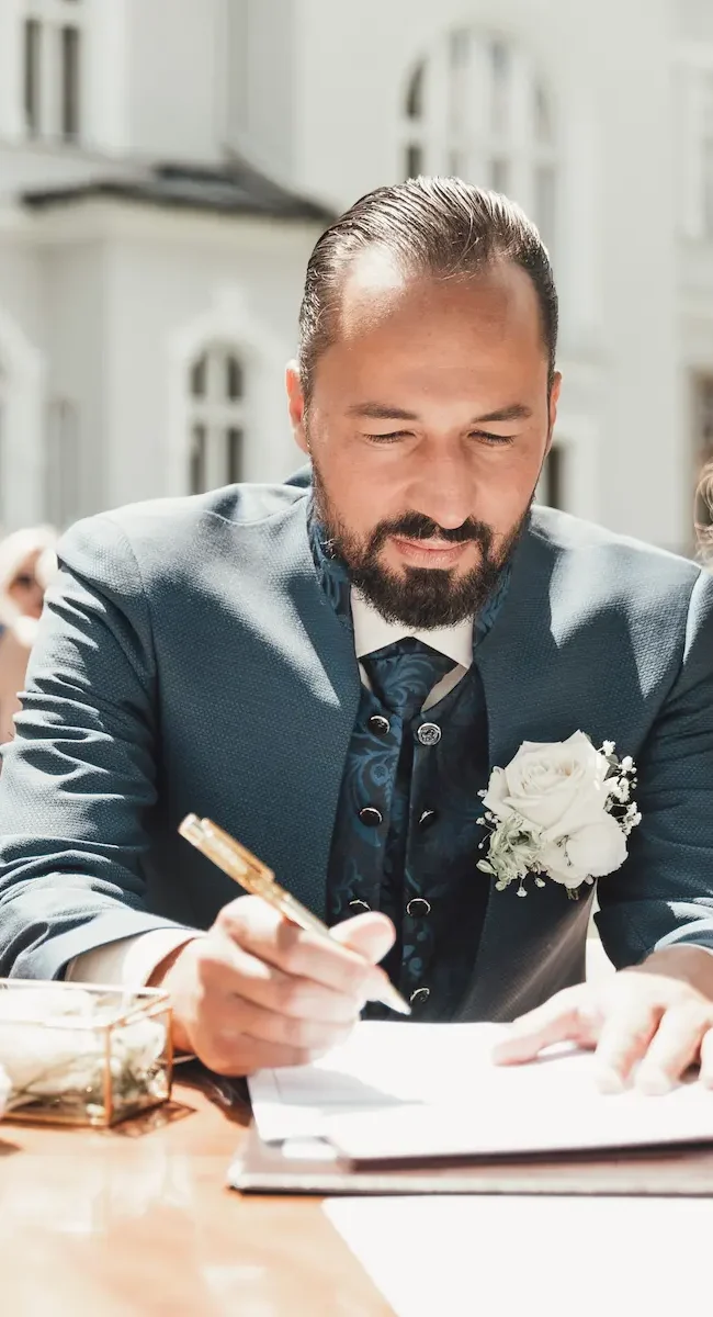 Bräutigam unterschreibt Hochzeitsdokument während der Trauung im eleganten Hochzeitsoutfit