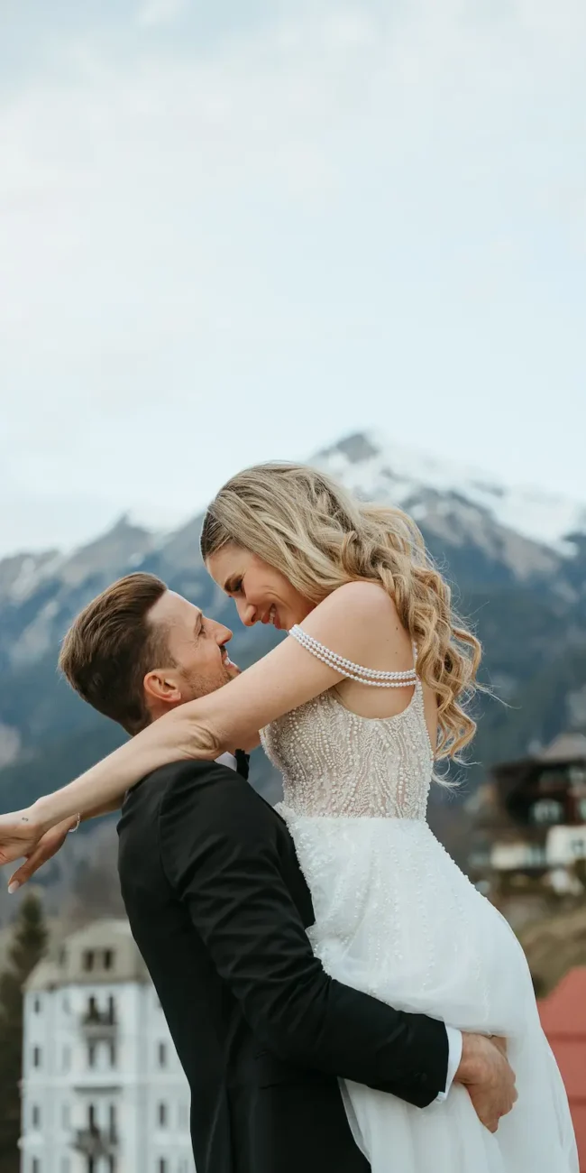 Bräutigam trägt seine Braut vor der Kulisse der Alpen in Bad Gastein